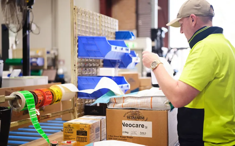 A worker in a high-visibility shirt preparing and labelling boxes at a packing station in a warehouse