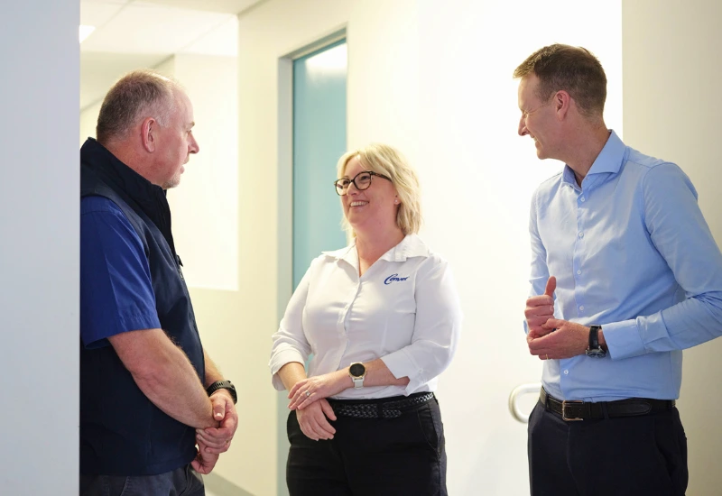 Three colleagues standing in a hallway having a friendly conversation, including a woman in a Cenvet shirt and two men in business attire